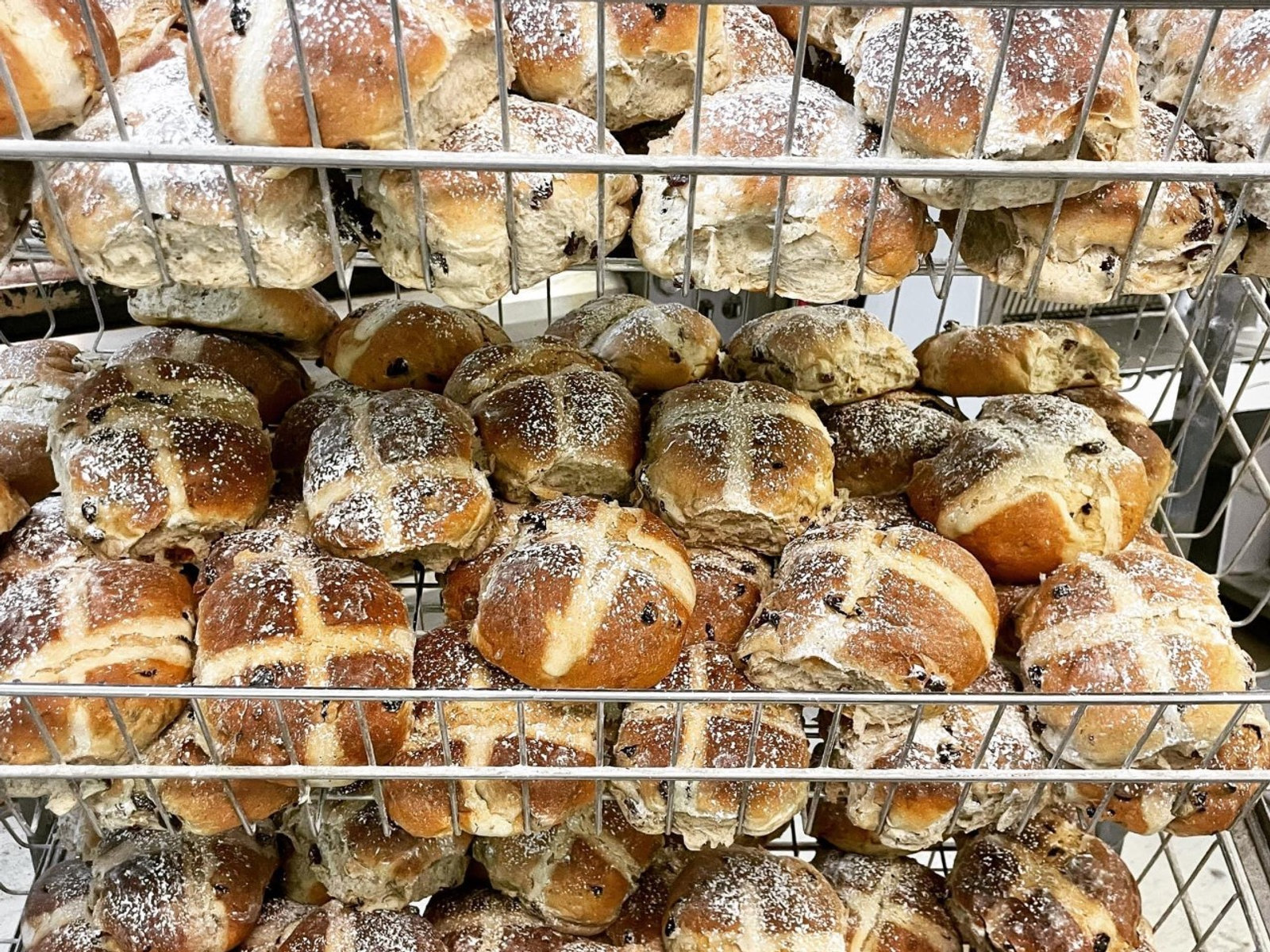 Wire racks stacked with sugar-dusted hot cross buns