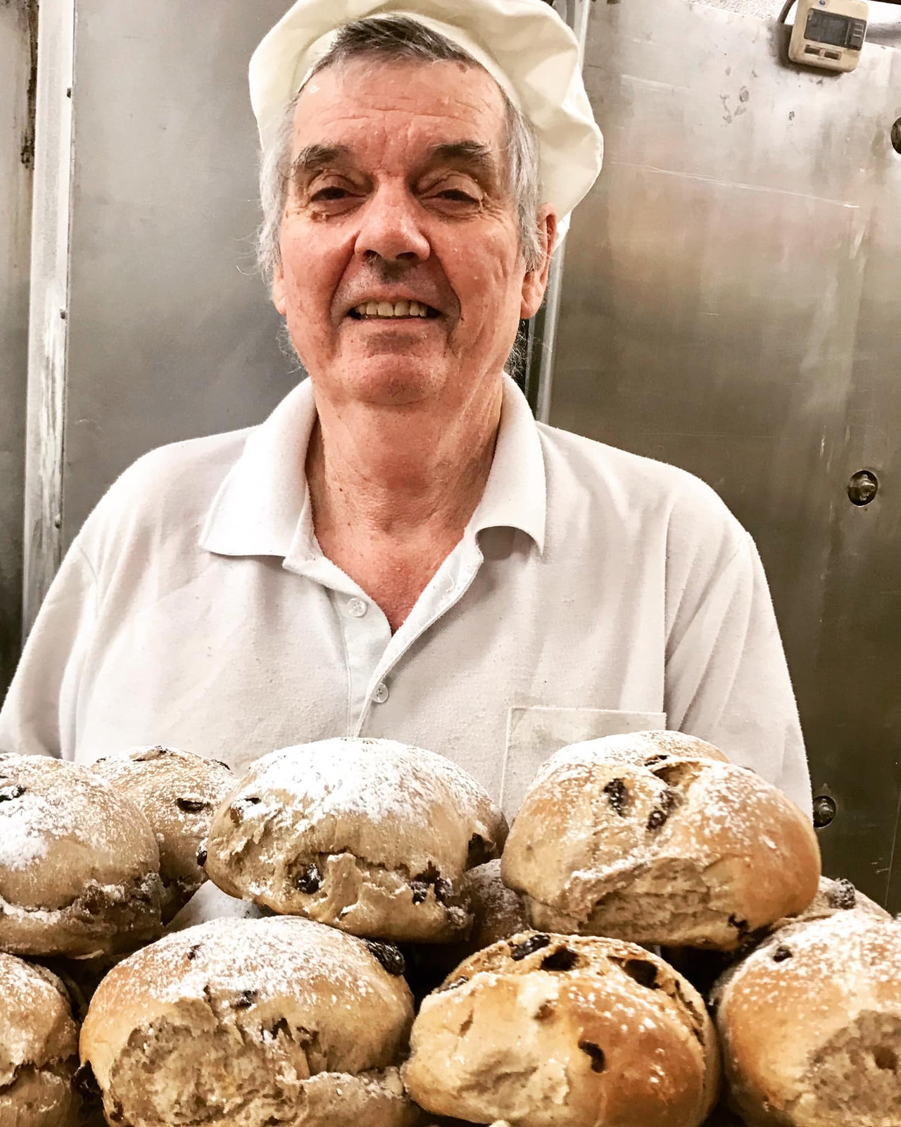 Danny Collins in his baker's hat behind a pile of sugar-dusted fruit buns